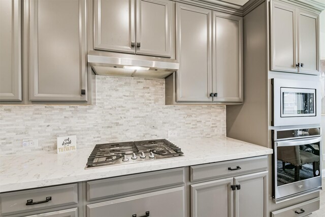 19303 Belmont Stakes Way, Tomball, TX 77377 - kitchen featuring under cabinet range hood, stainless steel appliances, gray cabinetry, tasteful backsplash, and light stone counters