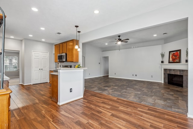 9515 Willow Crossing Dr, Houston, TX 77064 - kitchen featuring stainless steel microwave, brown cabinets, a ceiling fan, baseboards, and a tiled fireplace