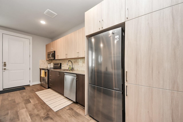 4819 Caroline St Unit 102, Houston, TX 77004 - kitchen featuring appliances with stainless steel finishes, light brown cabinets, wood finished floors, a sink, and decorative backsplash