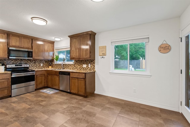 24 Wagon Lane Loop, Angleton, TX 77515 - kitchen with appliances with stainless steel finishes, backsplash, brown cabinetry, a sink, and baseboards