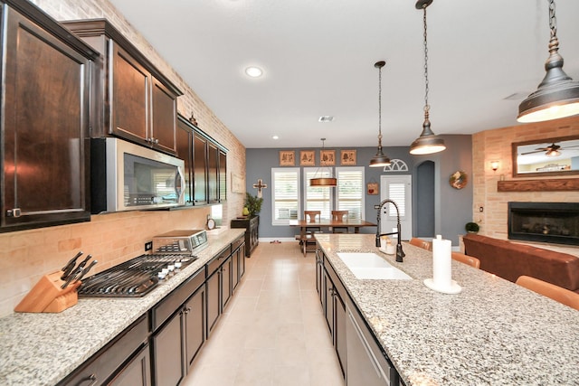 5131 Kingship Ct, Katy, TX 77493 - kitchen featuring stainless steel appliances, a sink, a fireplace, dark brown cabinets, and light stone countertops