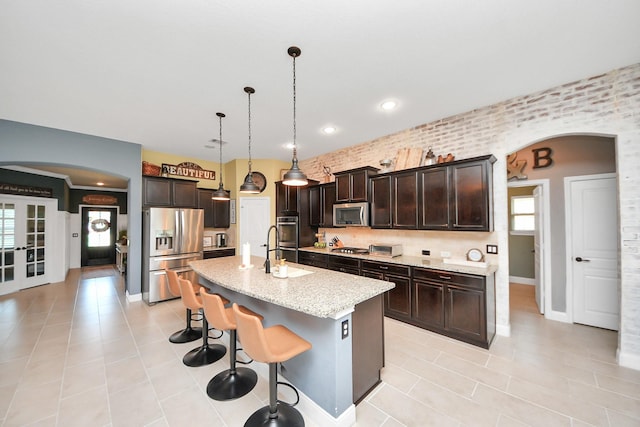 5131 Kingship Ct, Katy, TX 77493 - kitchen featuring stainless steel appliances, arched walkways, a sink, light tile patterned floors, and dark brown cabinetry