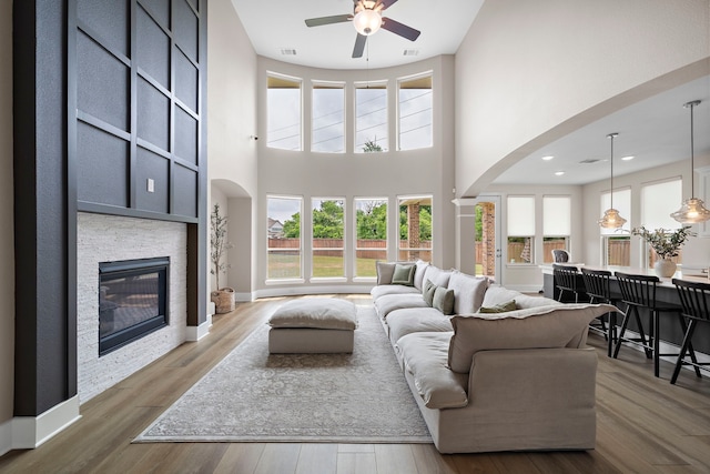 8211 Barristan Bluffs Ct, Magnolia, TX 77354 - living area featuring a ceiling fan, a fireplace, arched walkways, a high ceiling, and wood finished floors