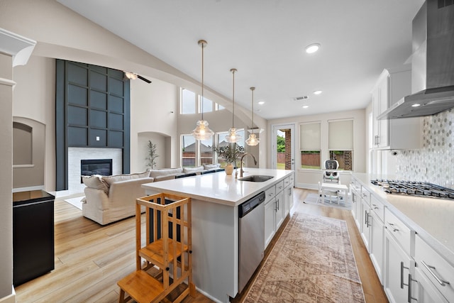 8211 Barristan Bluffs Ct, Magnolia, TX 77354 - kitchen with a sink, stainless steel appliances, wall chimney range hood, a fireplace, and light wood-type flooring