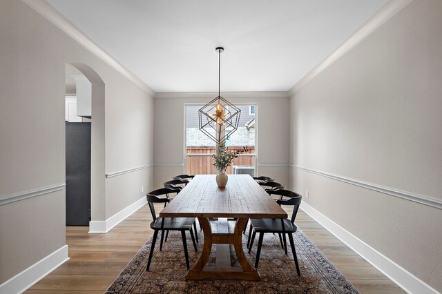 8211 Barristan Bluffs Ct, Magnolia, TX 77354 - dining area with arched walkways, baseboards, light wood-type flooring, crown molding, and a chandelier