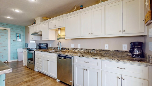1508 Galveston Ave, Port Bolivar, TX 77650 - kitchen featuring appliances with stainless steel finishes, under cabinet range hood, white cabinets, light wood-style flooring, and dark stone counters