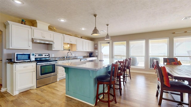1508 Galveston Ave, Port Bolivar, TX 77650 - kitchen featuring appliances with stainless steel finishes, under cabinet range hood, recessed lighting, white cabinets, and a kitchen breakfast bar