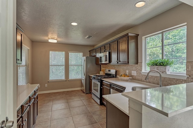 94 S Magnolia Pond Pl, The Woodlands, TX 77381 - kitchen with appliances with stainless steel finishes, a sink, light countertops, a textured ceiling, and dark brown cabinetry