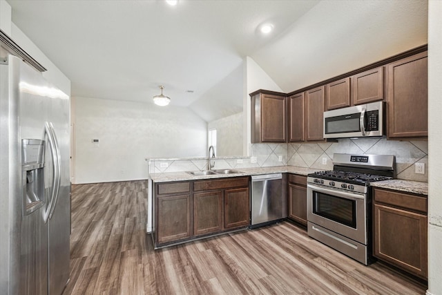 8931 Beacon Mill Dr, Cypress, TX 77433 - kitchen with appliances with stainless steel finishes, a sink, light wood-style floors, lofted ceiling, and a peninsula