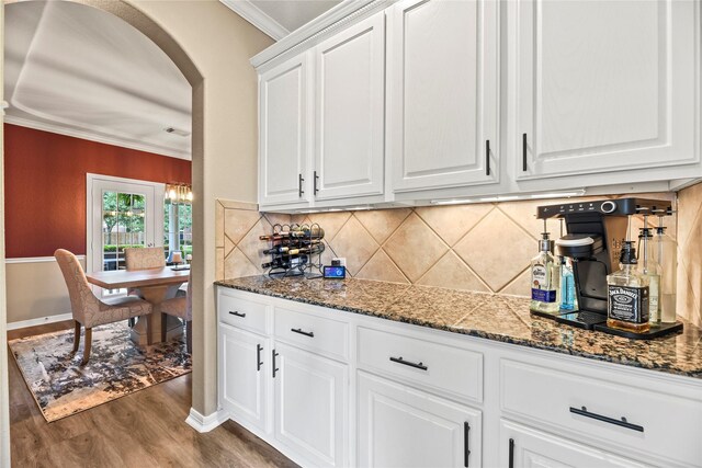 3707 Doyle Ct, Missouri City, TX 77459 - kitchen featuring wood finished floors, arched walkways, ornamental molding, white cabinetry, and backsplash