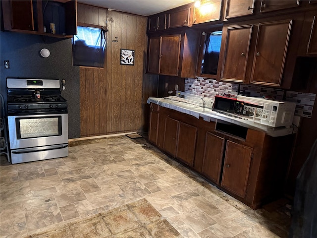 4204 Wipprecht St, Houston, TX 77026 - kitchen with stainless steel gas range, light stone finish floors, backsplash, dark brown cabinets, and wood walls