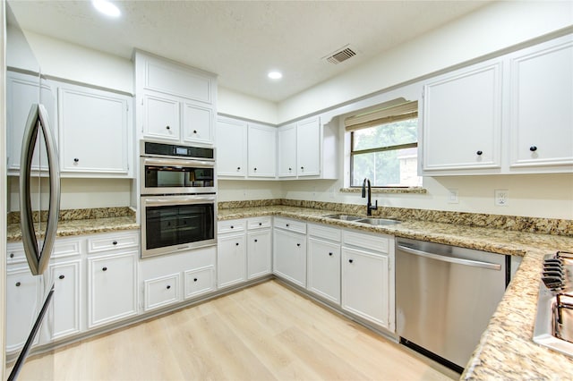 1715 Cobblestone Ct, Richmond, TX 77406 - kitchen featuring appliances with stainless steel finishes, a sink, white cabinetry, light wood-style floors, and recessed lighting