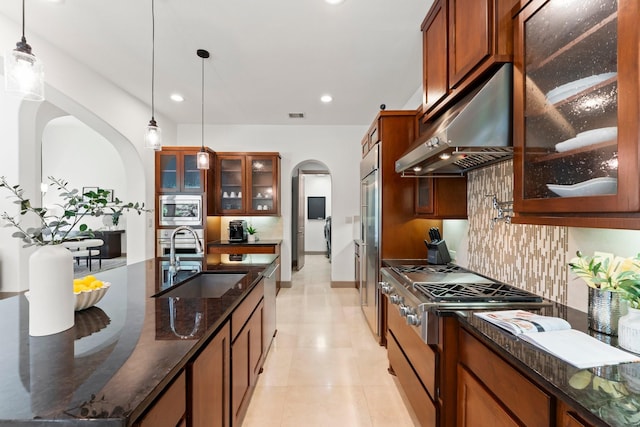 82 Valera Ridge Dr, Spring, TX 77389 - kitchen featuring under cabinet range hood, arched walkways, a sink, appliances with stainless steel finishes, and brown cabinetry