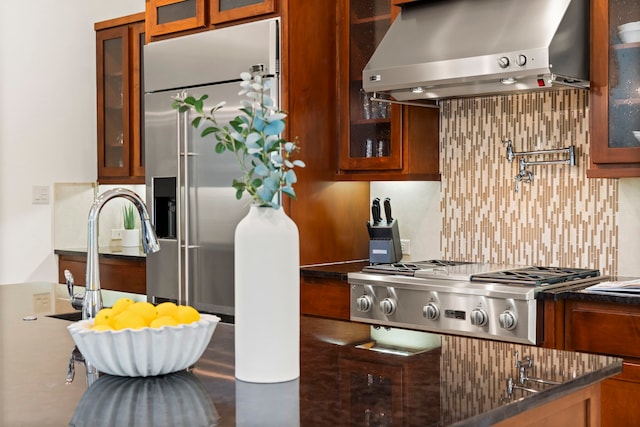 82 Valera Ridge Dr, Spring, TX 77389 - kitchen featuring wall chimney exhaust hood, stainless steel appliances, glass insert cabinets, decorative backsplash, and brown cabinetry