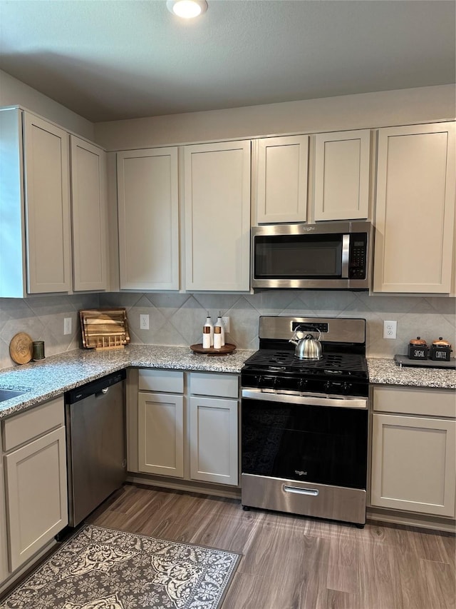 13556 Bowfin Dr, Conroe, TX 77384 - kitchen with appliances with stainless steel finishes, backsplash, wood finished floors, and light stone countertops