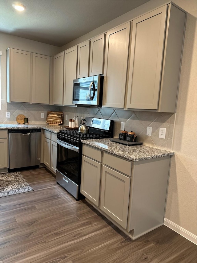 13556 Bowfin Dr, Conroe, TX 77384 - kitchen with appliances with stainless steel finishes, decorative backsplash, dark wood-type flooring, baseboards, and light stone countertops
