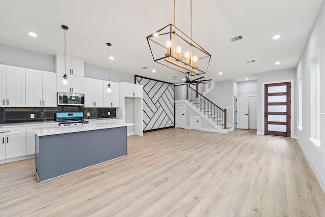 6631 Foster St, Houston, TX 77021 - kitchen with appliances with stainless steel finishes, backsplash, white cabinetry, light wood finished floors, and a chandelier