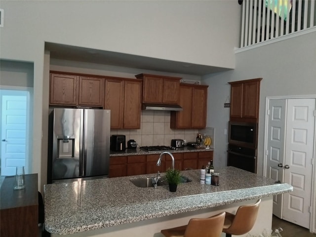 3619 Dry Creek Dr, Missouri City, TX 77459 - kitchen featuring stainless steel appliances, a sink, brown cabinets, backsplash, and under cabinet range hood