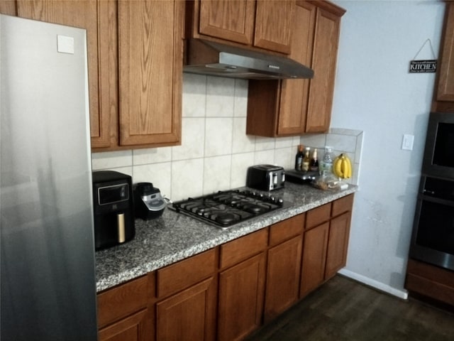 3619 Dry Creek Dr, Missouri City, TX 77459 - kitchen featuring appliances with stainless steel finishes, under cabinet range hood, tasteful backsplash, brown cabinets, and dark wood finished floors