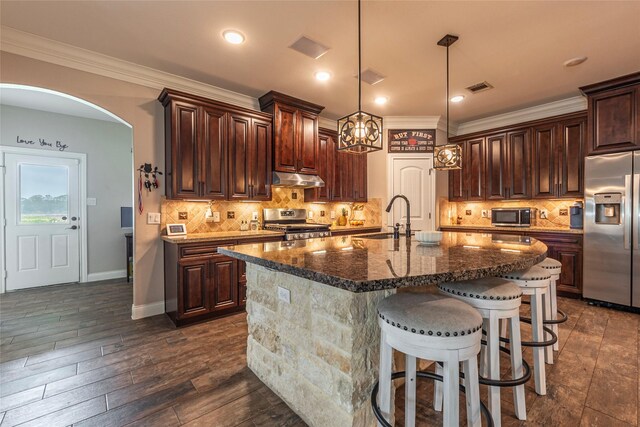 2323 Foley Rd, Crosby, TX 77532 - kitchen with appliances with stainless steel finishes, under cabinet range hood, a breakfast bar, dark brown cabinetry, and dark stone countertops