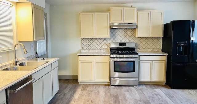 1602 W Blum St, Alvin, TX 77511 - kitchen featuring appliances with stainless steel finishes, under cabinet range hood, a sink, light wood finished floors, and tasteful backsplash