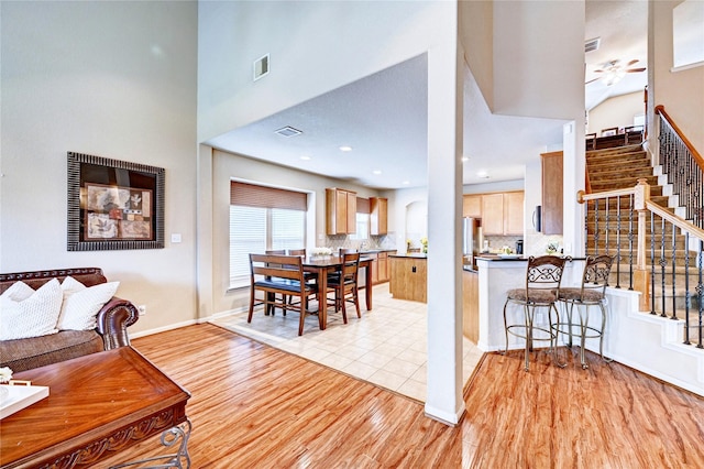 5838 Deleon Trail Dr, Spring, TX 77379 - living room featuring stairway, light wood-type flooring, a towering ceiling, ceiling fan, and baseboards