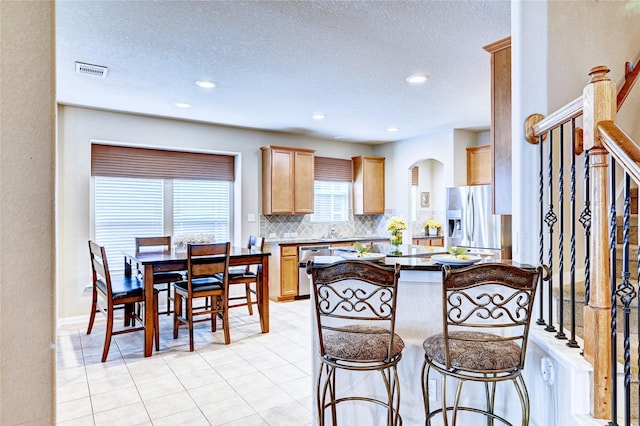 5838 Deleon Trail Dr, Spring, TX 77379 - kitchen with stainless steel appliances, decorative backsplash, a kitchen breakfast bar, a textured ceiling, and light tile patterned flooring