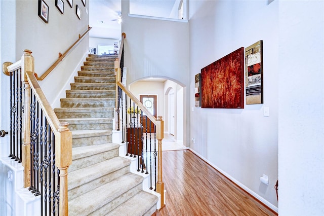 5838 Deleon Trail Dr, Spring, TX 77379 - stairway featuring arched walkways, wood finished floors, a towering ceiling, a ceiling fan, and baseboards