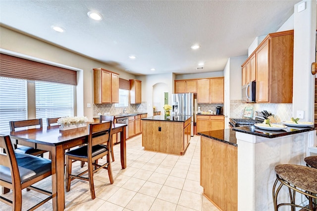 5838 Deleon Trail Dr, Spring, TX 77379 - kitchen featuring stainless steel appliances, decorative backsplash, a kitchen island, dark stone counters, and light tile patterned floors