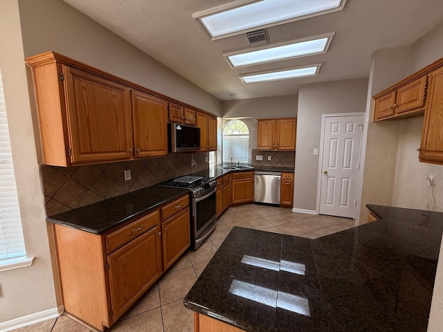 9619 Therrell Dr, Houston, TX 77064 - kitchen featuring stainless steel appliances, a sink, backsplash, light tile patterned flooring, and brown cabinetry