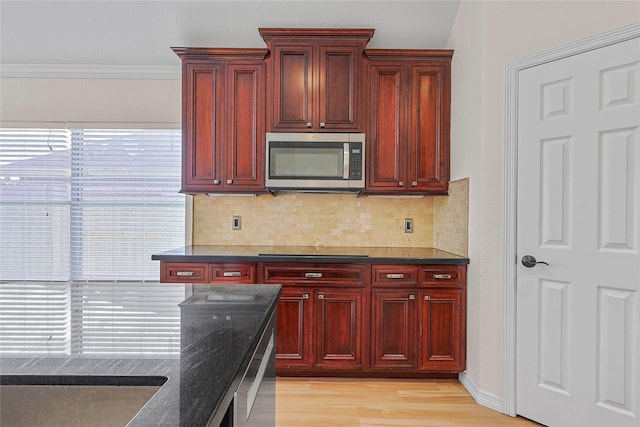 4907 Sundance Hollow Ln, Katy, TX 77494 - kitchen with stainless steel microwave, dark brown cabinets, light wood-style flooring, backsplash, and dark stone countertops