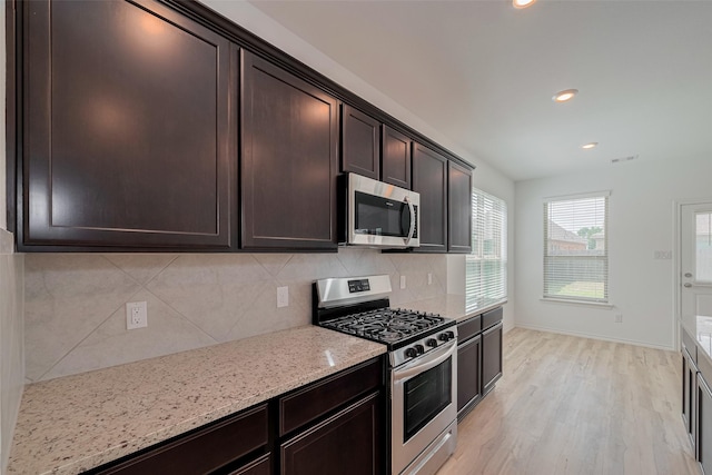 23922 Olivenza Trl, New Caney, TX 77357 - kitchen with appliances with stainless steel finishes, tasteful backsplash, dark brown cabinetry, light stone countertops, and light wood-style floors