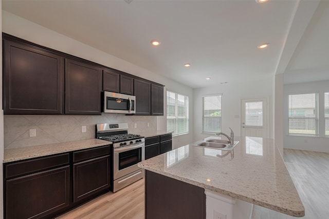 23922 Olivenza Trl, New Caney, TX 77357 - kitchen featuring stainless steel appliances, light wood-style flooring, tasteful backsplash, dark brown cabinets, and a kitchen island with sink