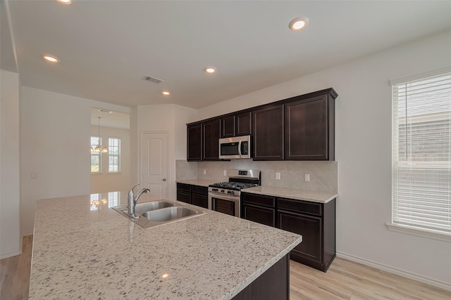 23922 Olivenza Trl, New Caney, TX 77357 - kitchen featuring appliances with stainless steel finishes, light wood-style floors, decorative backsplash, dark brown cabinets, and an island with sink