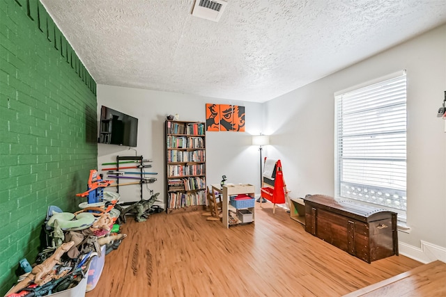 2307 Jackson Ln, League City, TX 77573 - rec room with a textured ceiling, light wood-style flooring, and brick wall