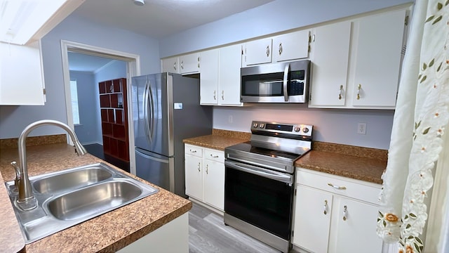 13419 Greenway Dr, Sugar Land, TX 77498 - kitchen featuring appliances with stainless steel finishes, a sink, white cabinets, light wood-style flooring, and dark countertops
