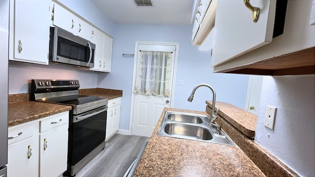 13419 Greenway Dr, Sugar Land, TX 77498 - kitchen with stainless steel appliances, a sink, wood finished floors, white cabinetry, and dark countertops