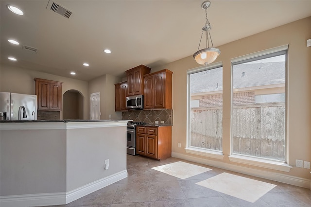 4131 Regal Stone Ln, Sugar Land, TX 77479 - kitchen featuring appliances with stainless steel finishes, backsplash, dark countertops, arched walkways, and hanging light fixtures