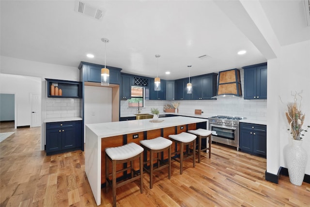 701 W 39th St, Houston, TX 77018 - kitchen with stainless steel stove, premium range hood, blue cabinets, tasteful backsplash, and light wood-type flooring