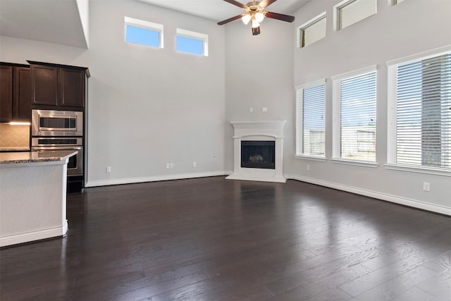4926 Thunder Creek Ln, Sugar Land, TX 77479 - unfurnished living room featuring a towering ceiling, a ceiling fan, dark wood-style flooring, a fireplace with raised hearth, and baseboards