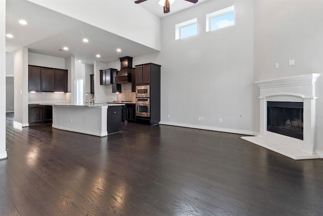4926 Thunder Creek Ln, Sugar Land, TX 77479 - unfurnished living room featuring a ceiling fan, a towering ceiling, dark wood-style flooring, a fireplace with raised hearth, and baseboards