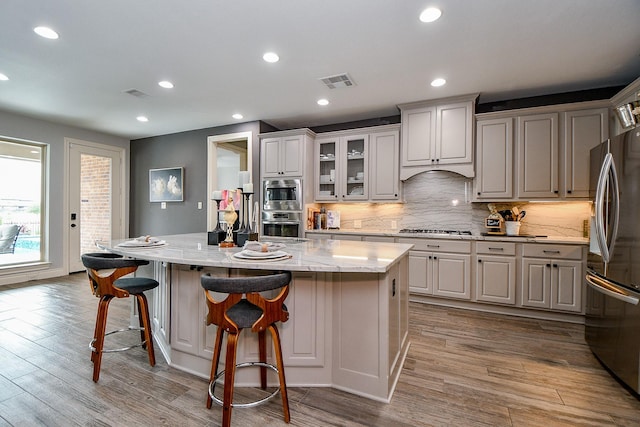 29016 Concan Crossing Ct, Katy, TX 77494 - kitchen featuring appliances with stainless steel finishes, backsplash, a kitchen bar, wood finished floors, and light stone countertops