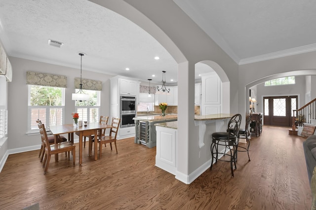 7 Newland Ct, The Woodlands, TX 77382 - kitchen featuring dark wood-style floors, a breakfast bar, stainless steel double oven, white cabinetry, and light stone counters