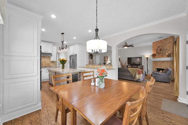 7 Newland Ct, The Woodlands, TX 77382 - dining space featuring a ceiling fan, light wood finished floors, arched walkways, recessed lighting, and a large fireplace