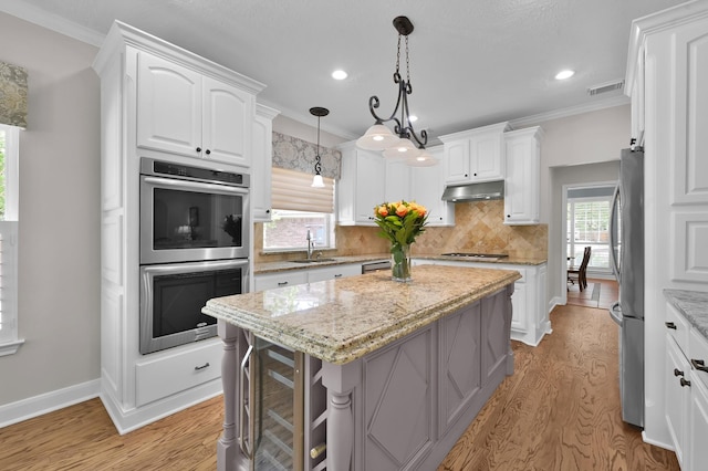 7 Newland Ct, The Woodlands, TX 77382 - kitchen featuring stainless steel appliances, under cabinet range hood, ornamental molding, a kitchen island, and backsplash