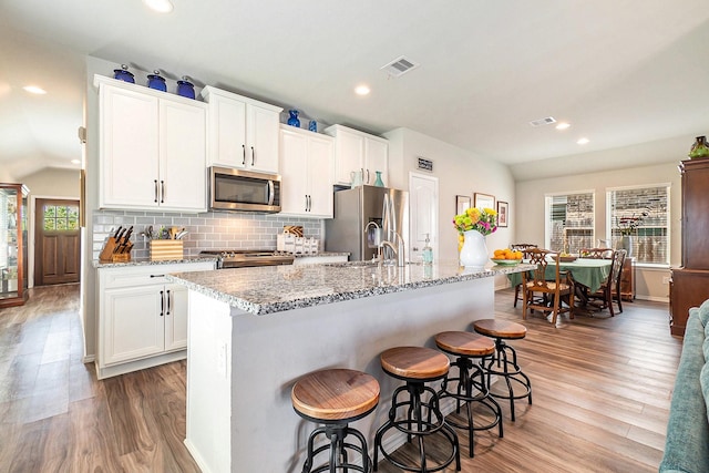 9521 Mountain Maple Pl, Conroe, TX 77385 - kitchen with appliances with stainless steel finishes, light wood-style floors, an island with sink, a kitchen breakfast bar, and recessed lighting