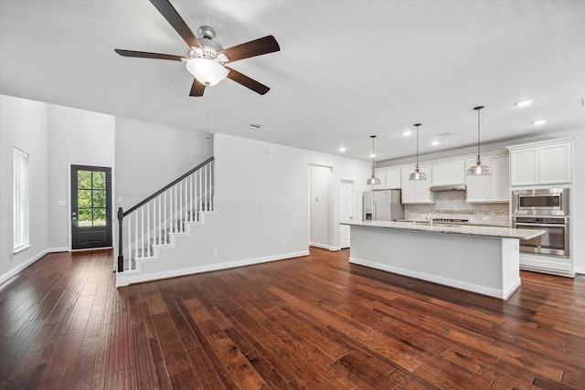 12 Centennial Ridge Pl, Magnolia, TX 77354 - kitchen featuring stainless steel appliances, a center island with sink, ceiling fan, dark wood-type flooring, and light stone countertops