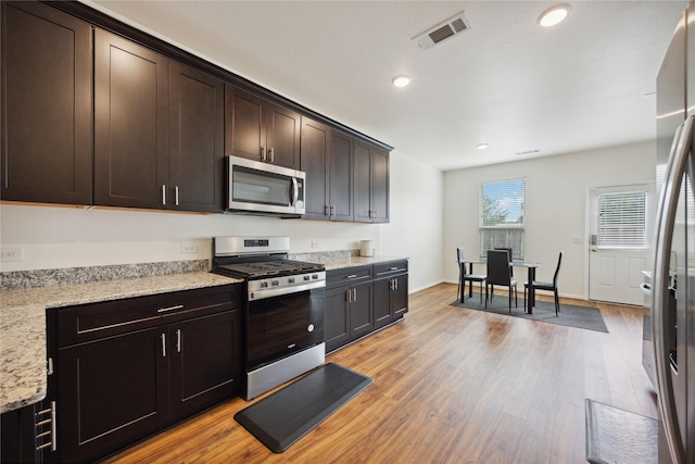 10127 Clearwick St, Houston, TX 77034 - kitchen featuring stainless steel appliances, light wood-style floors, recessed lighting, dark brown cabinetry, and light stone counters