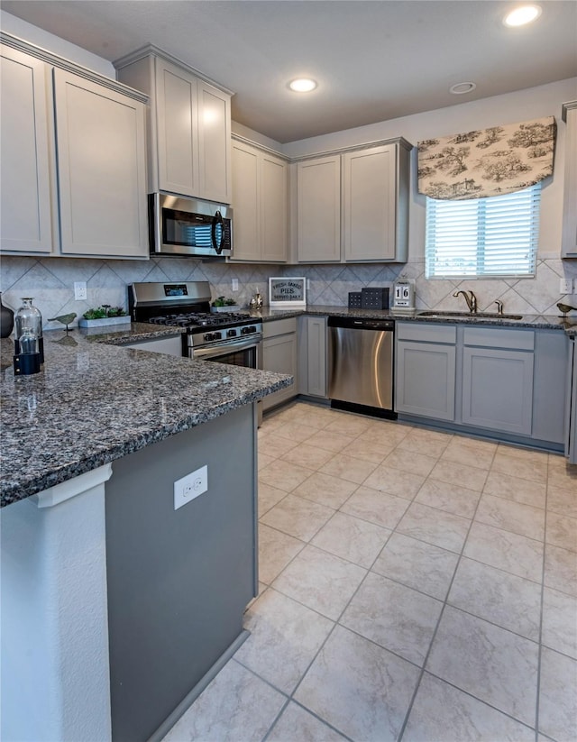 214 Emerald Thicket Ln, Humble, TX 77336 - kitchen with appliances with stainless steel finishes, a sink, gray cabinetry, backsplash, and dark stone countertops