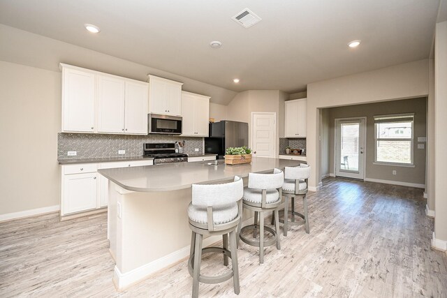 11210 Victoria Hollow Trce, Richmond, TX 77406 - kitchen with stainless steel appliances, a kitchen island with sink, decorative backsplash, light wood-type flooring, and white cabinets